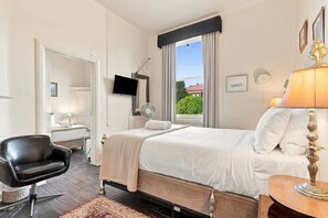 A hotel room with a bed, a desk, a chair, a TV, a window with curtains, and a lamp. - Edinburgh Family Room (Hobart)