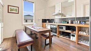 Une cuisine compacte avec une table et un banc en bois, un four encastré, un four à micro-ondes et un petit réfrigérateur.