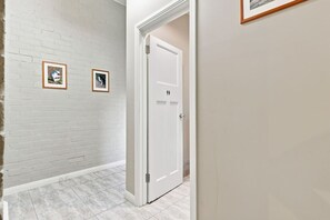 A hallway with a white brick wall, two framed pictures, a white door, and a tiled floor. - Edinburgh Family Room (Hobart)