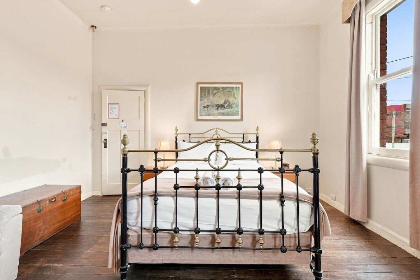 A bedroom with a metal bed frame, a wooden bench, a door, and a window with a view.