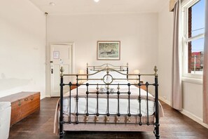A bedroom with a metal bed frame, a wooden bench, a door, and a window with a view. - Edinburgh Premium Room + Ensuite (Hobart)