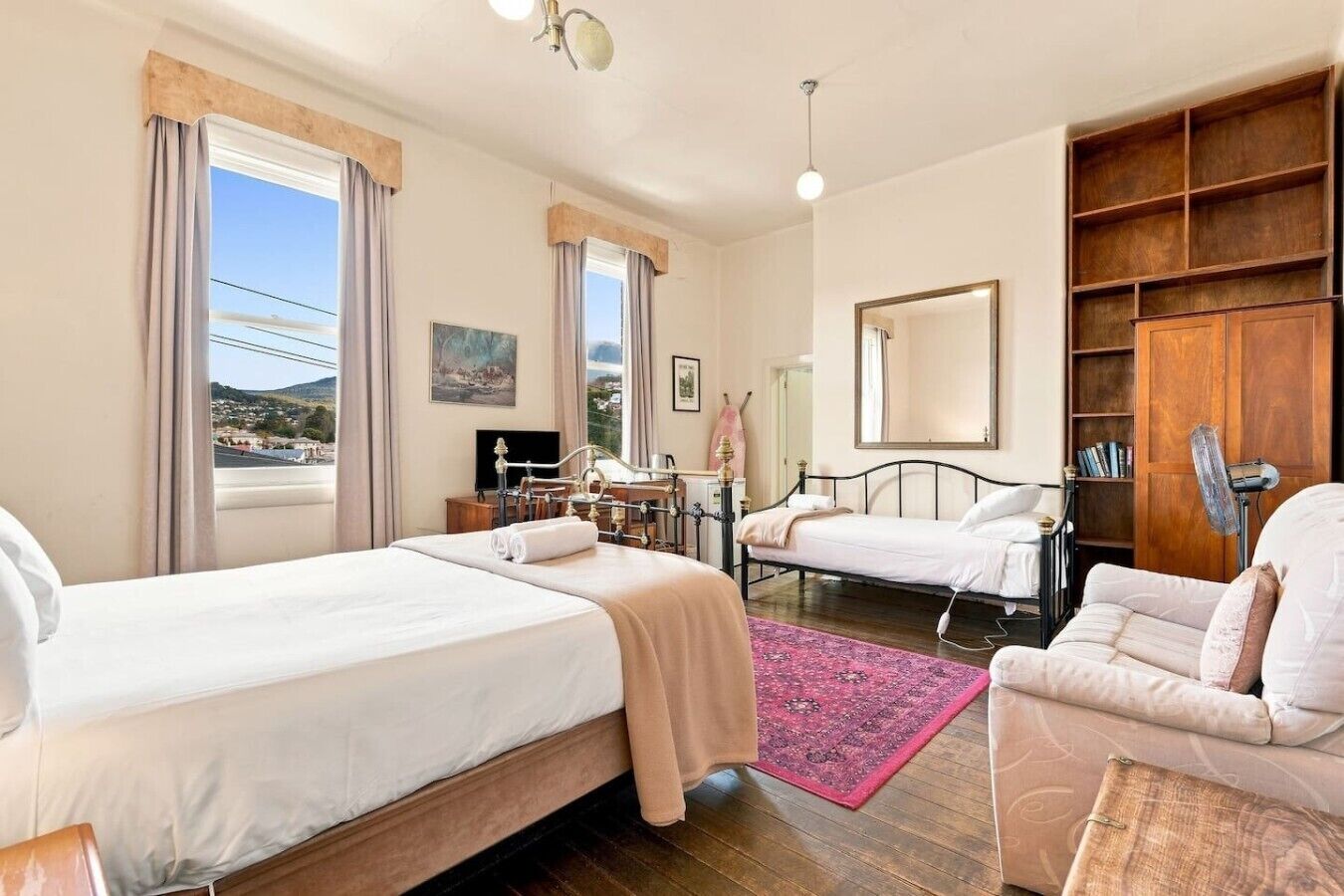 Habitación de hotel con dos camas, un escritorio, una silla, una estantería y un amplio ventanal con cortinas.