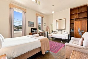 A hotel room with two beds, a desk, a chair, a bookshelf, and a large window with curtains. - Edinburgh Premium Room + Ensuite (Hobart)