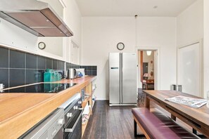 A compact kitchen with a stove, oven, refrigerator, and a wooden dining table with a bench. - Edinburgh Premium Room + Ensuite (Hobart)