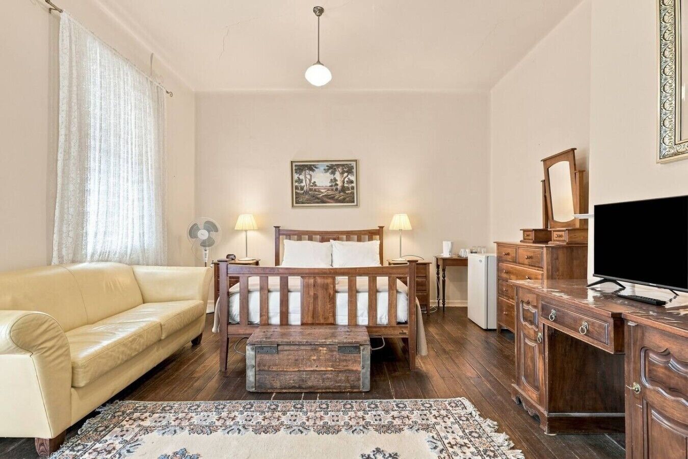 A bedroom with a wooden bed, a sofa, a desk with a television, and a dresser.