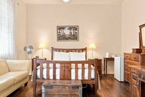A bedroom with a wooden bed, bedside lamps, a small table, a dresser, and a refrigerator. - Edinburgh Deluxe Family Suite + Ensuite (Hobart)