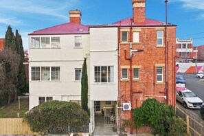 A two-story building with a red roof, a white facade, and a brick section. There is a car parked in front, and a sign indicating a car park. - Edinburgh Queen & Single Rm + Ensuite (Hobart)