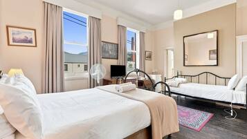 A hotel room with two beds, a TV, a fan, and a large window with curtains.