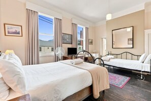 Quarto de hotel com duas camas, televisão, ventoinha e uma janela grande com cortinas.