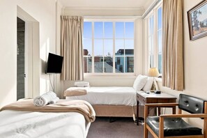 A hotel room with two beds, a desk, a chair, a television, and a window with curtains. - Edinburgh Twin Room with Ensuite (Hobart)