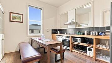 A compact kitchen with a wooden table and bench, a built-in oven, microwave, and a small refrigerator.
