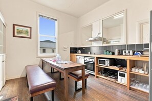 A compact kitchen with a wooden table and bench, a built-in oven, microwave, and a small refrigerator. - Edinburgh Twin Room with Ensuite (Hobart)