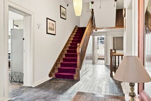 A staircase with a wooden handrail and purple carpet, leading to a room with a white door and a lamp on a table. - Edinburgh Twin Room with Ensuite (Hobart)