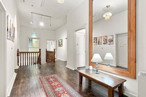 A spacious hallway with wooden flooring, a red patterned rug, a wooden bench, and a large mirror. - Edinburgh Twin Room with Ensuite (Hobart)