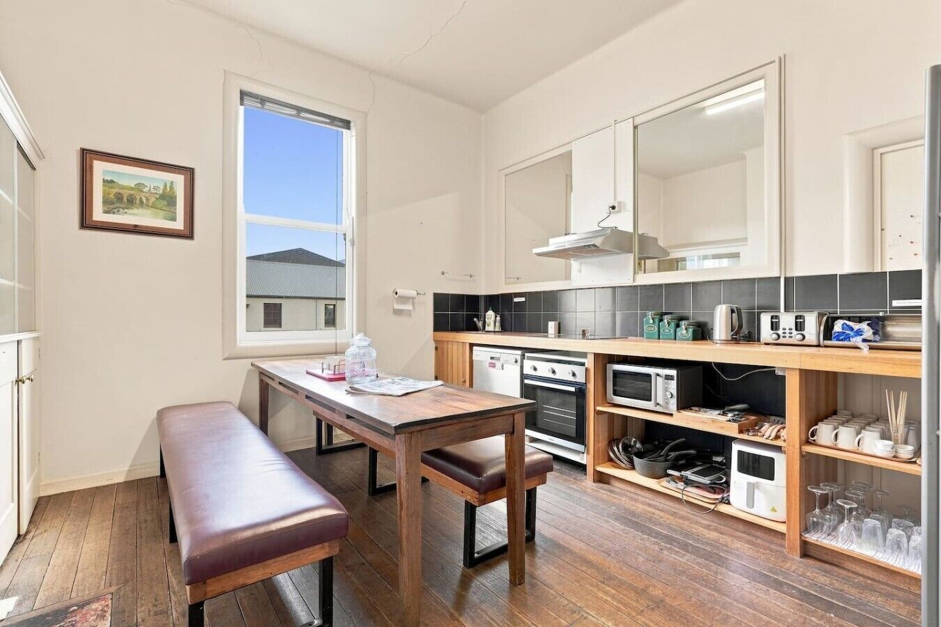 A compact kitchen with a wooden table and bench, a built-in oven, microwave, and a small refrigerator.