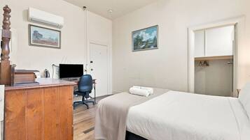 A hotel room with a wooden desk, a computer, a chair, two beds, a wardrobe, and two framed pictures on the wall.