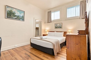 A bedroom with a bed, bedside lamps, a wooden dresser, a painting on the wall, and a window with curtains. - Edinburgh Family + Ensuite | Hobart CBD (Hobart)