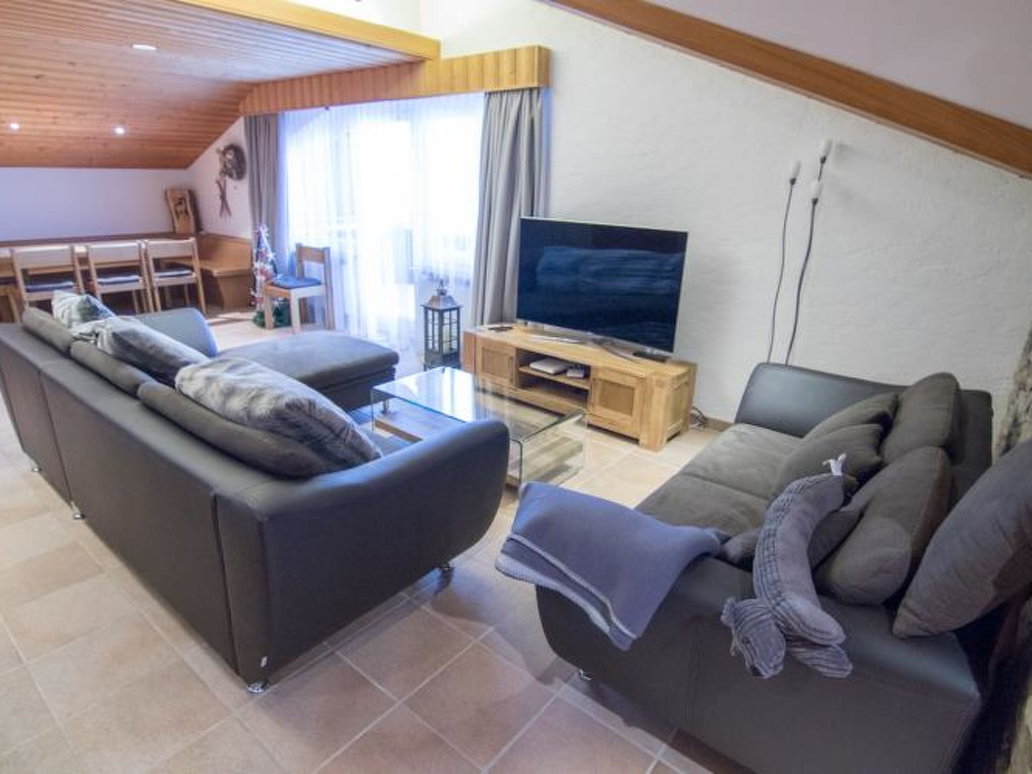 A modern living room with a sofa, a smaller couch, a TV stand, and a dining area with a table and chairs.