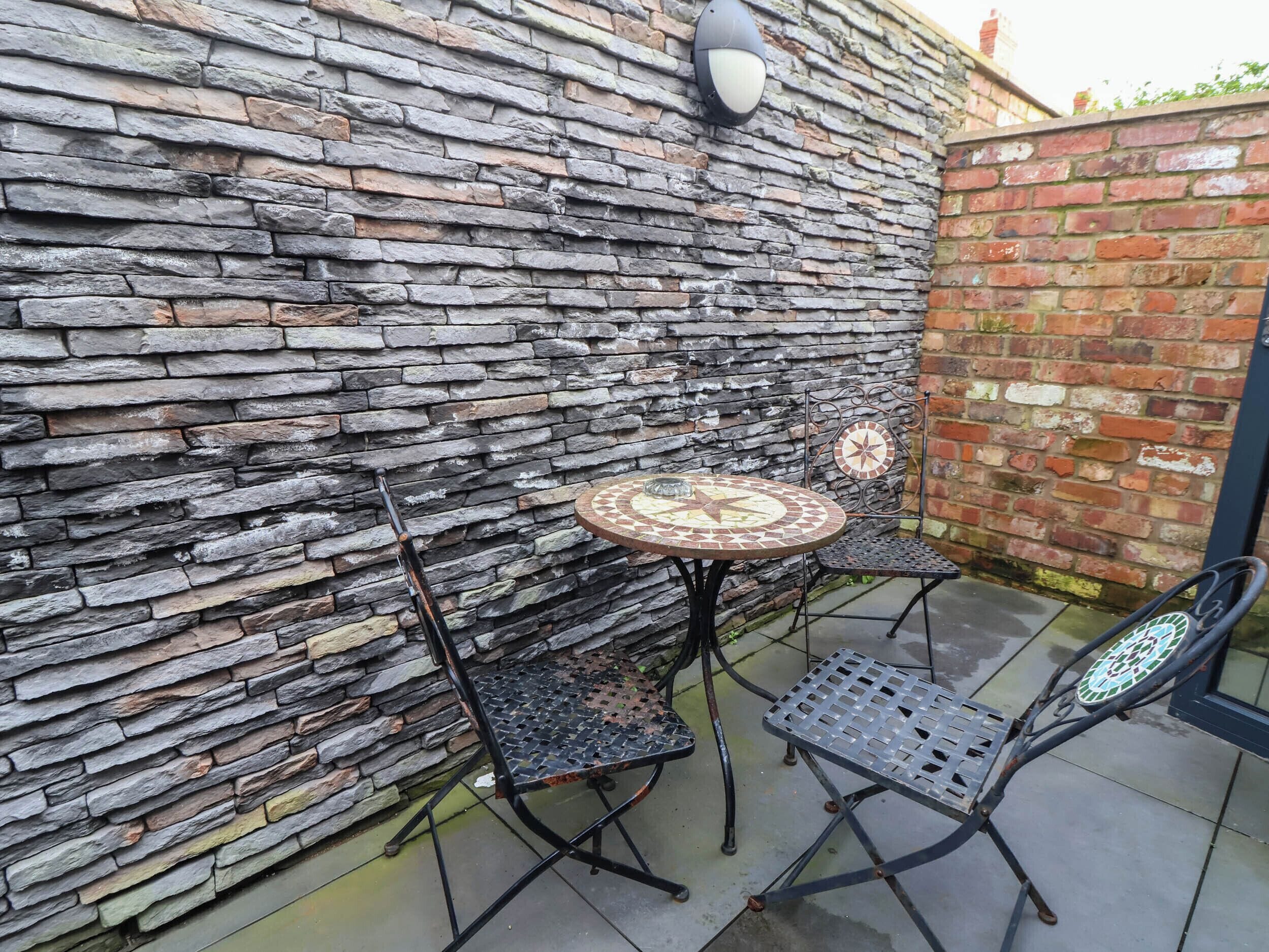 A patio area with a stone wall, two metal chairs, and a small round table.
