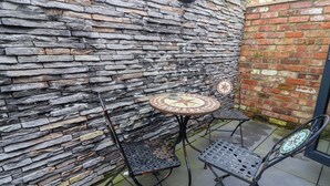 A patio area with a stone wall, two metal chairs, and a small round table.