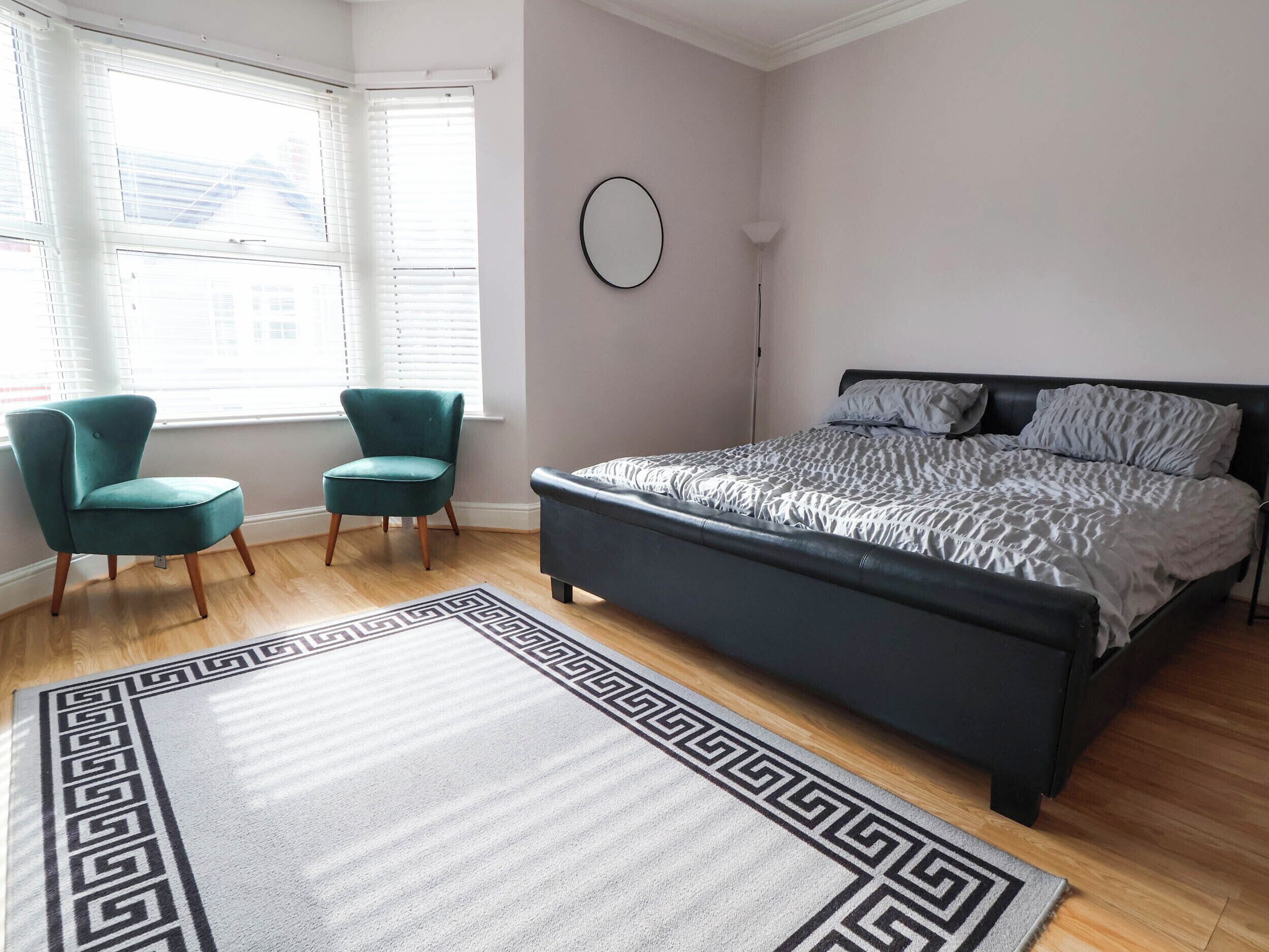 A bedroom with a bed, two chairs, a rug, and a window with blinds.