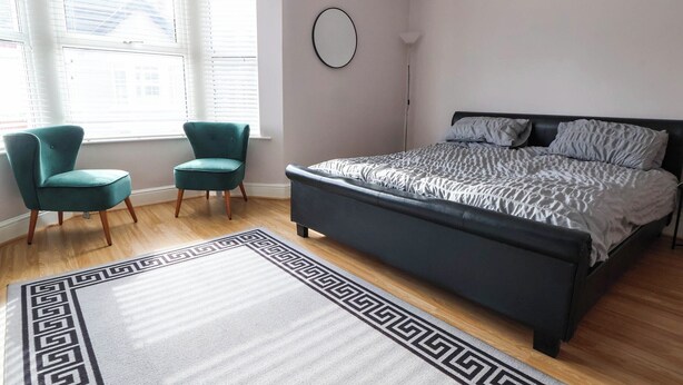 A bedroom with a bed, two chairs, a rug, and a window with blinds.