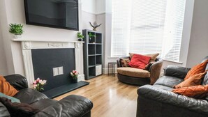 A living room with a fireplace, two sofas, a TV mounted on the wall, and a window with blinds.