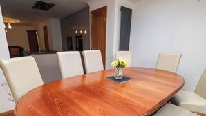 A dining area with a wooden oval table, six white chairs, and a vase with yellow flowers.