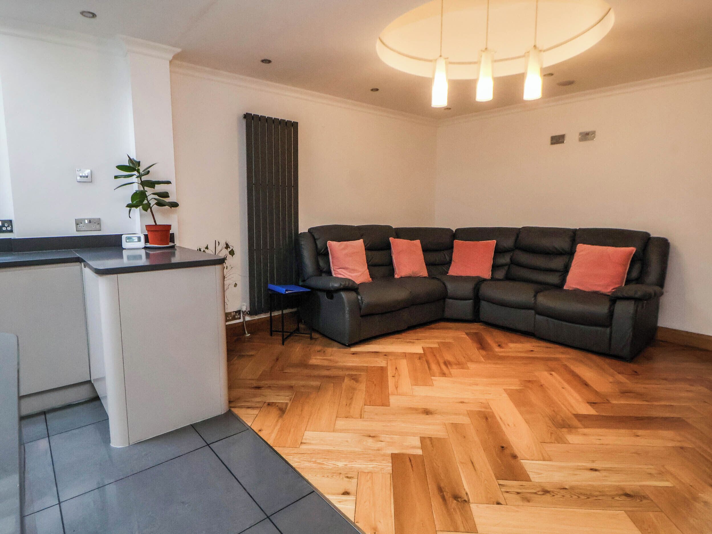 Una sala de estar moderna con un sofá de cuero negro, una pequeña zona de cocina y un suelo de madera con diseño espiga.