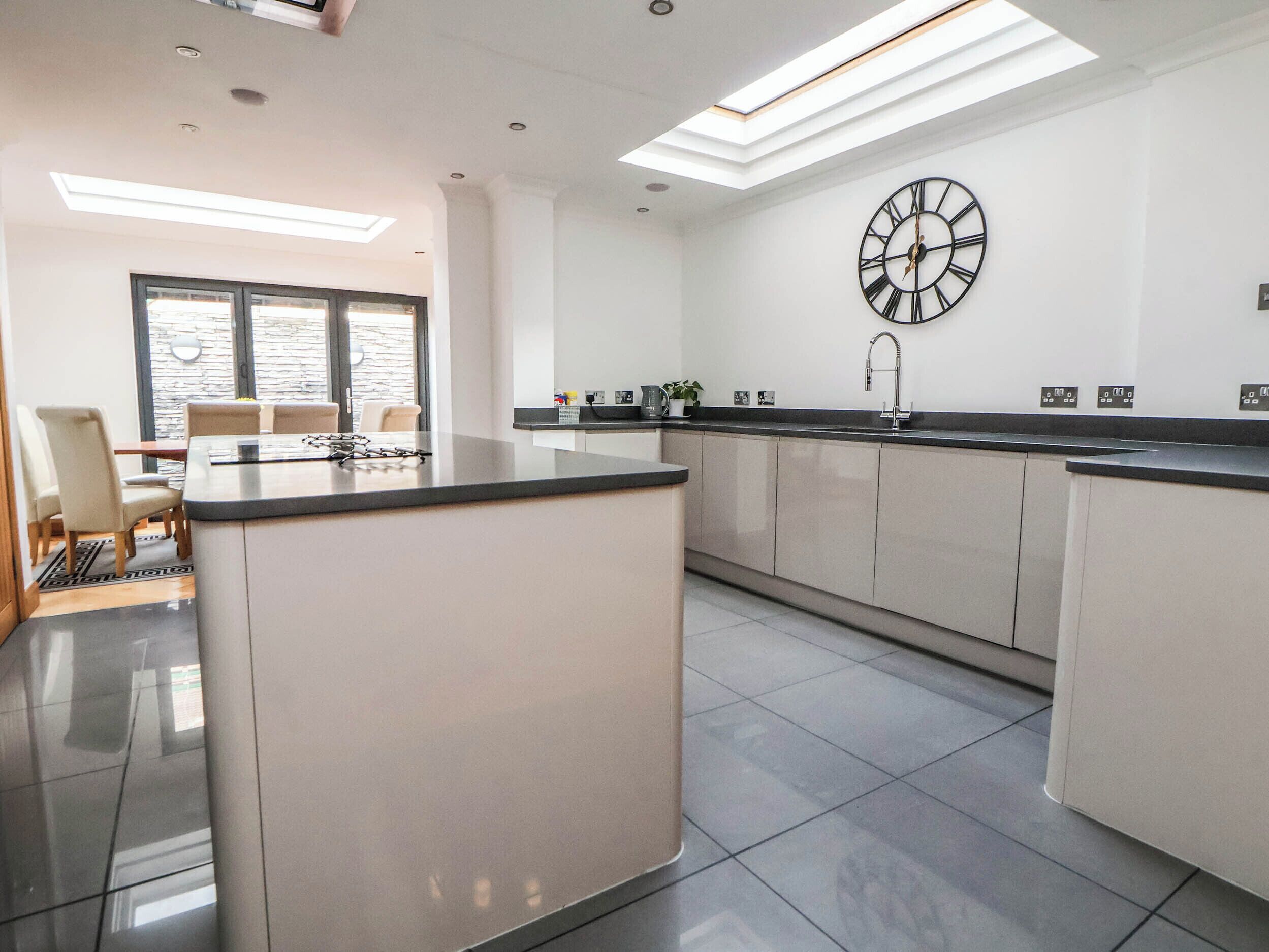 Una cocina moderna con una isla central, un reloj de pared grande y un comedor con sillas.