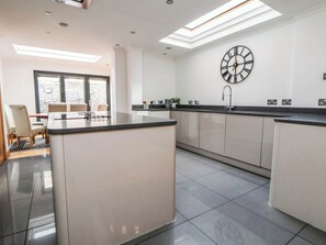 Una cocina moderna con una isla central, un reloj de pared grande y un comedor con sillas.