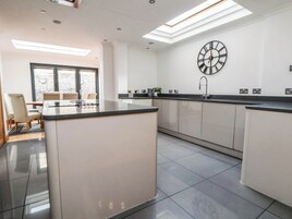 Una cocina moderna con una isla central, un reloj de pared grande y un comedor con sillas.
