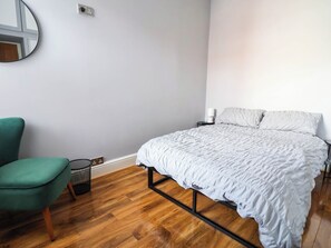 Un dormitorio con cama, una silla, una mesita de noche y un espejo instalado en la pared.