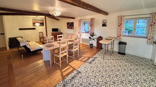 Un vaste espace de vie doté d’un plafond en bois, d’une table à manger avec des chaises, d’un canapé, d’un téléviseur et d’une fenêtre avec des rideaux.