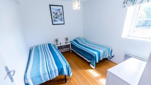 Une chambre avec deux lits, une petite table, un radiateur et une fenêtre.