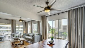A spacious living room with a high ceiling, a ceiling fan, a dining table, and a view of the city through large windows. - Waikiki Penthouse, 1 Free Parking, 3bdrm, Sleeps 6 (Honolulu)