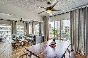 A spacious living room with a high ceiling, a ceiling fan, a dining table, and a view of the city through large windows. - Waikiki Penthouse, 1 Free Parking, 3bdrm, Sleeps 6 (Honolulu)