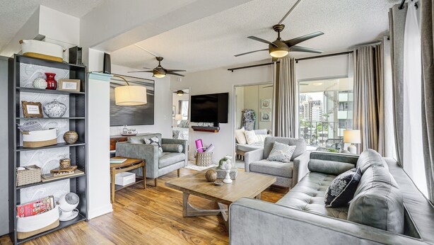 A modern living room with a sofa, coffee table, and a bookshelf. There is a ceiling fan and a TV mounted on the wall. - Waikiki Penthouse, 1 Free Parking, 3bdrm, Sleeps 6 (Honolulu)