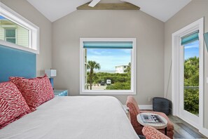A bedroom with a large bed, a view of the beach, and a small table with a magazine. - A Salty Mate (Beach House Escape Guest House) (Gulf Shores)