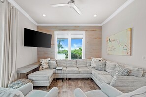 Un salon moderne avec un canapé d’angle, un téléviseur à écran plat fixé au mur et une grande fenêtre donnant sur un paysage verdoyant.