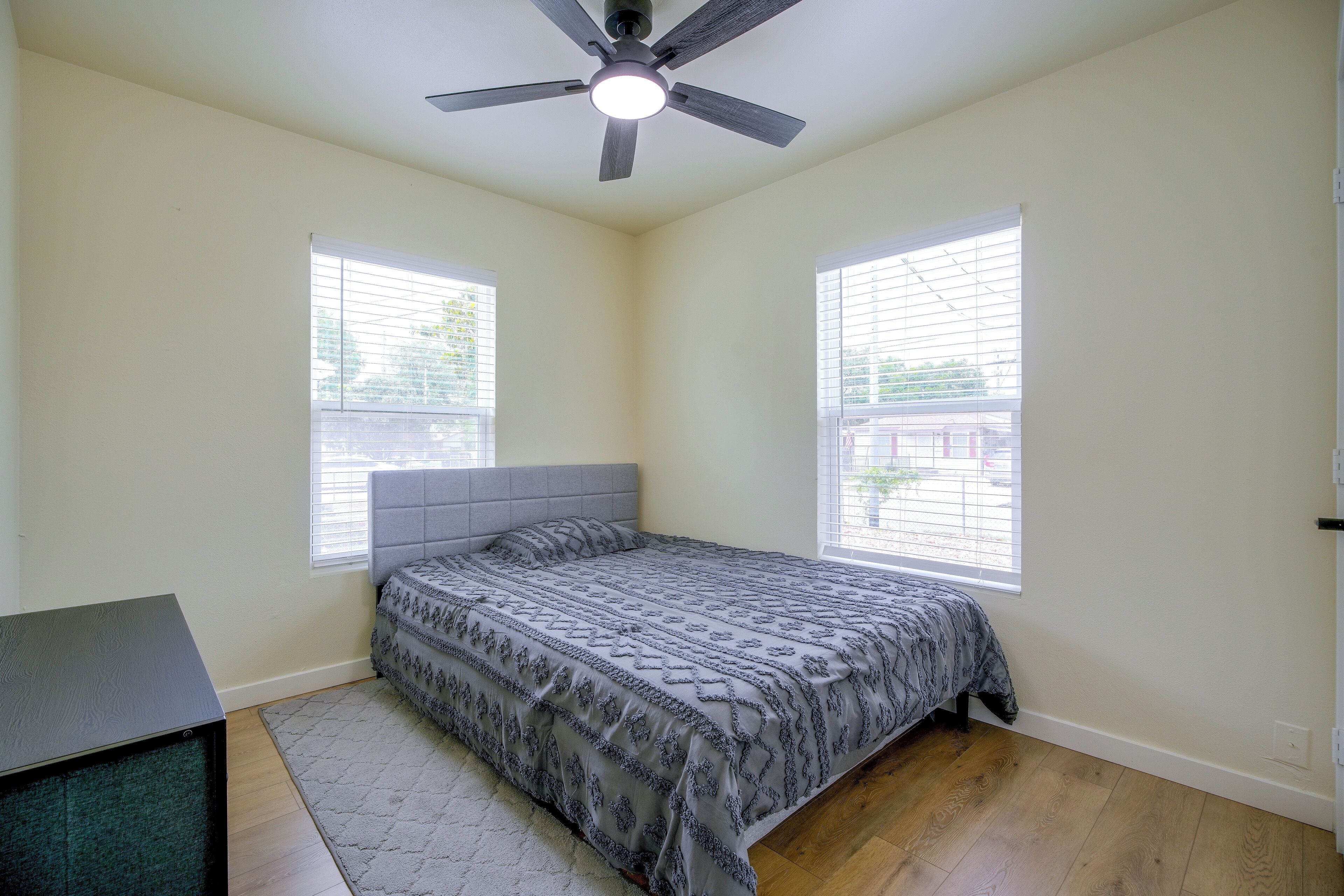 Un dormitorio con cama, ventilador de techo y dos ventanas con persianas.