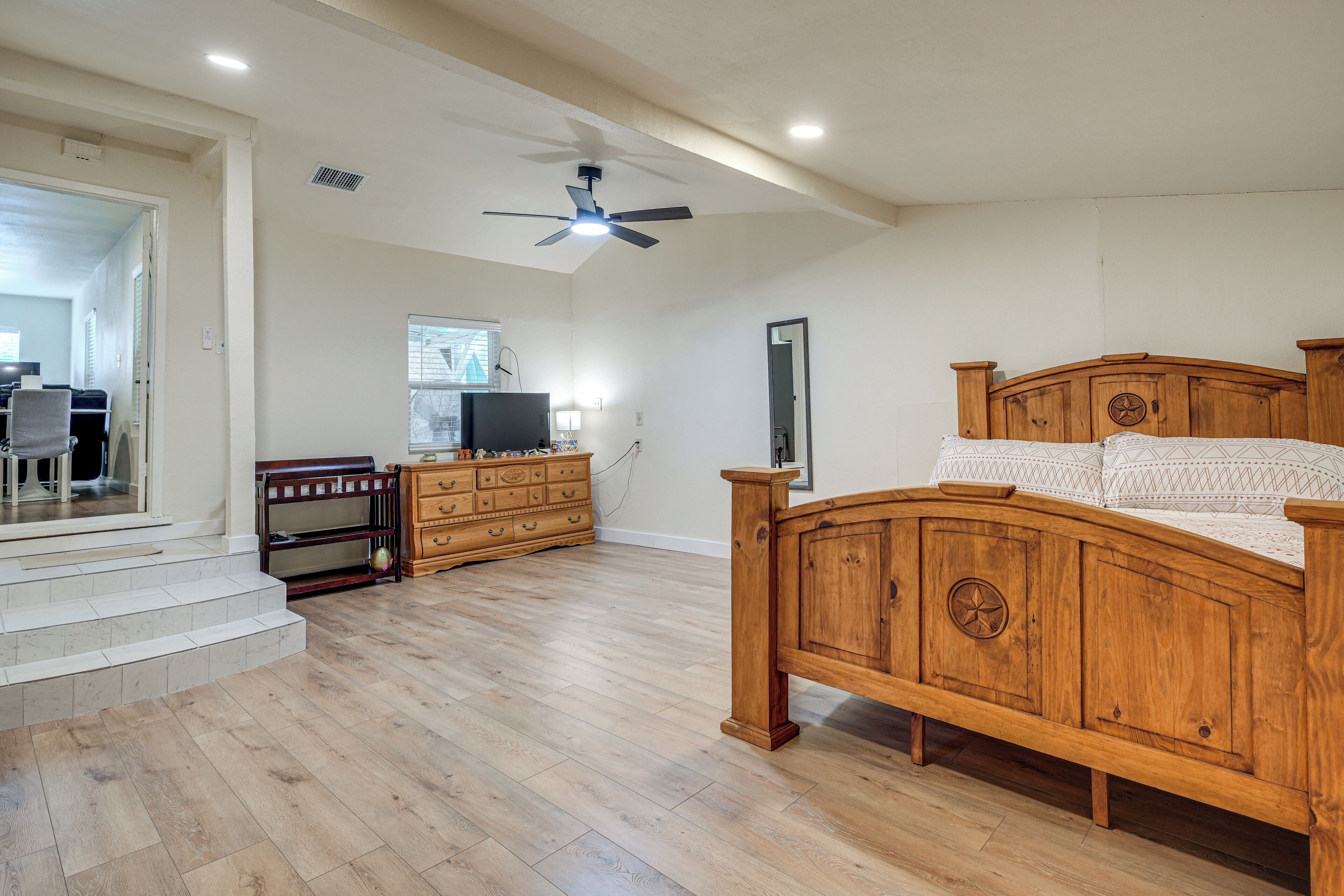 A spacious bedroom with a wooden bed, a dresser, a television, and a ceiling fan.
