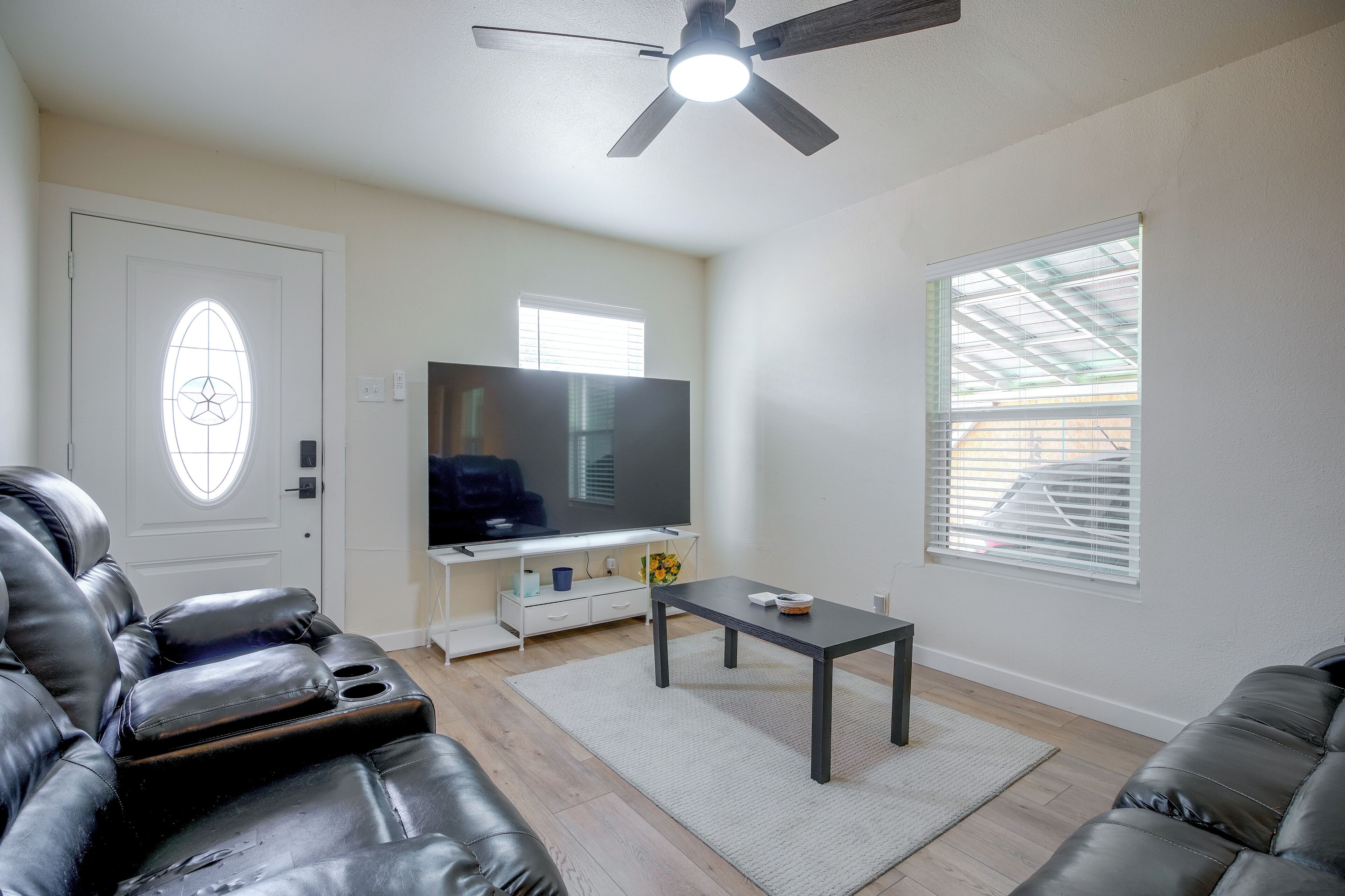 A living room with a television, leather sofas, a coffee table, and a ceiling fan.
