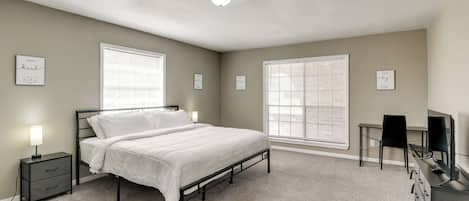 A bedroom with a bed, bedside tables, a desk with a chair, and large windows.
