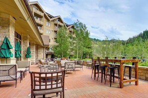 A hotel patio with outdoor seating, stone walls, and a view of a forested hillside. - Ski-in/ski-out! Mtn-view Montage Deer Valley Condo (Park City)