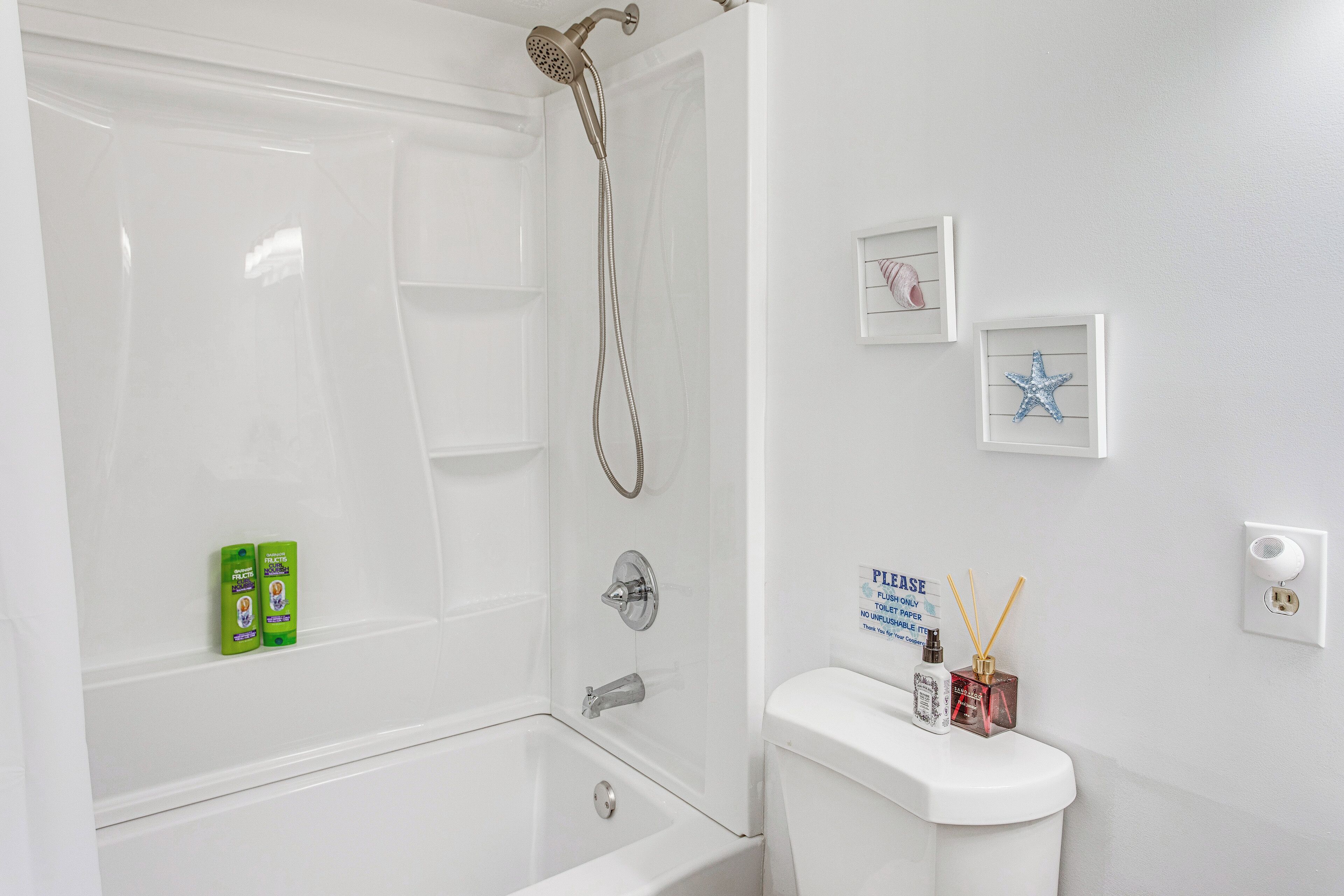 A bathroom with a bathtub, toilet, and a showerhead. There are two framed pictures on the wall and a sign above the toilet.