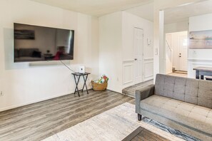 Ein Wohnzimmer mit flachbildfernseher an der Wand, einem grauen Sofa, einem kleinen schwarzen Beistelltisch und einem gewebten Korb auf dem Boden.