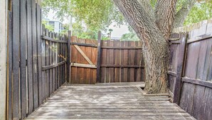 A wooden deck leading to a gated area with a tree trunk in the center. - Steps to Sea & Sand! Family Haven in Myrtle Beach (Myrtle Beach)