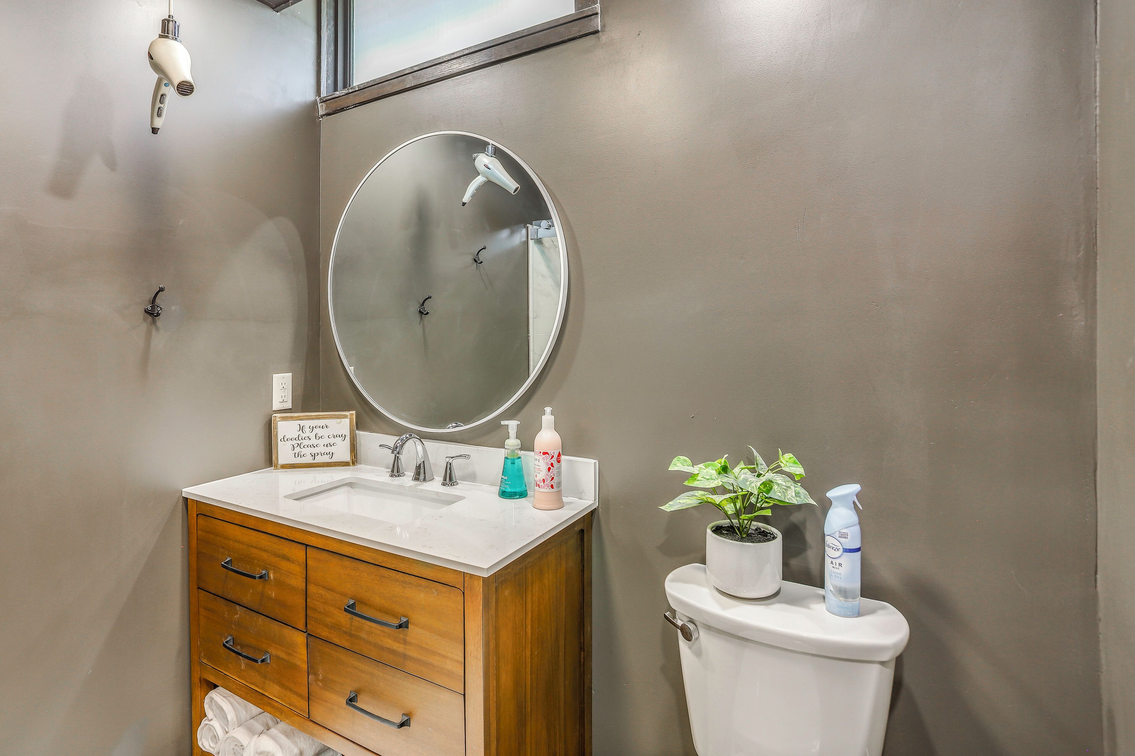A bathroom with a wooden vanity, a round mirror, a toilet, and a wall-mounted towel rack.