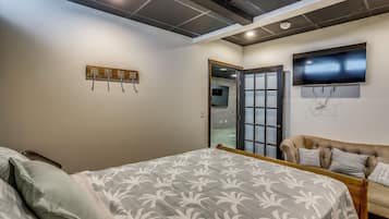 A bedroom with a bed, a sofa, a TV, and a ceiling with recessed lighting.